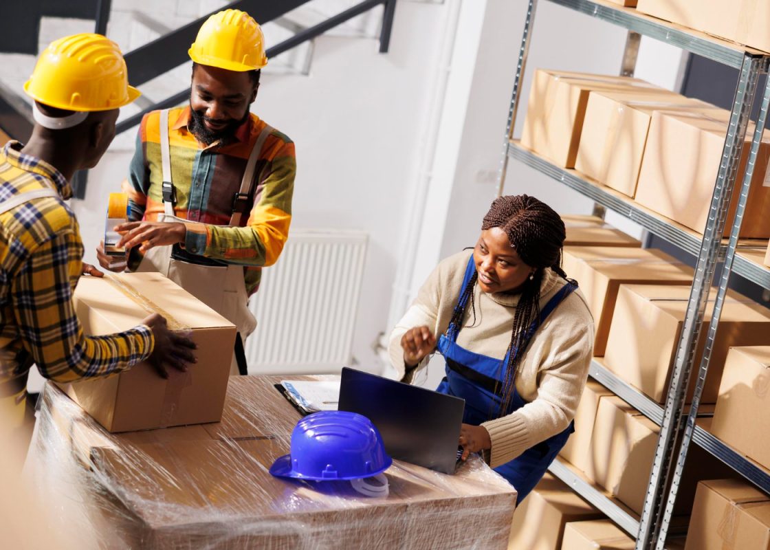 Warehouse Manager Checking Orders List Coordinating Parcels Packing Process African American Woman Supervisor With Laptop Controlling Freight Cardboard Boxes Sealing Dispatching