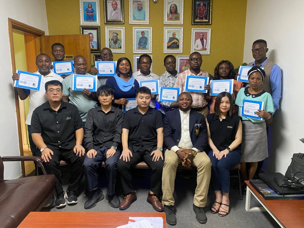 Diverse group of coworkers posing in an office, holding blue certificate folders, after a certificate ceremony on a couch and standing area.